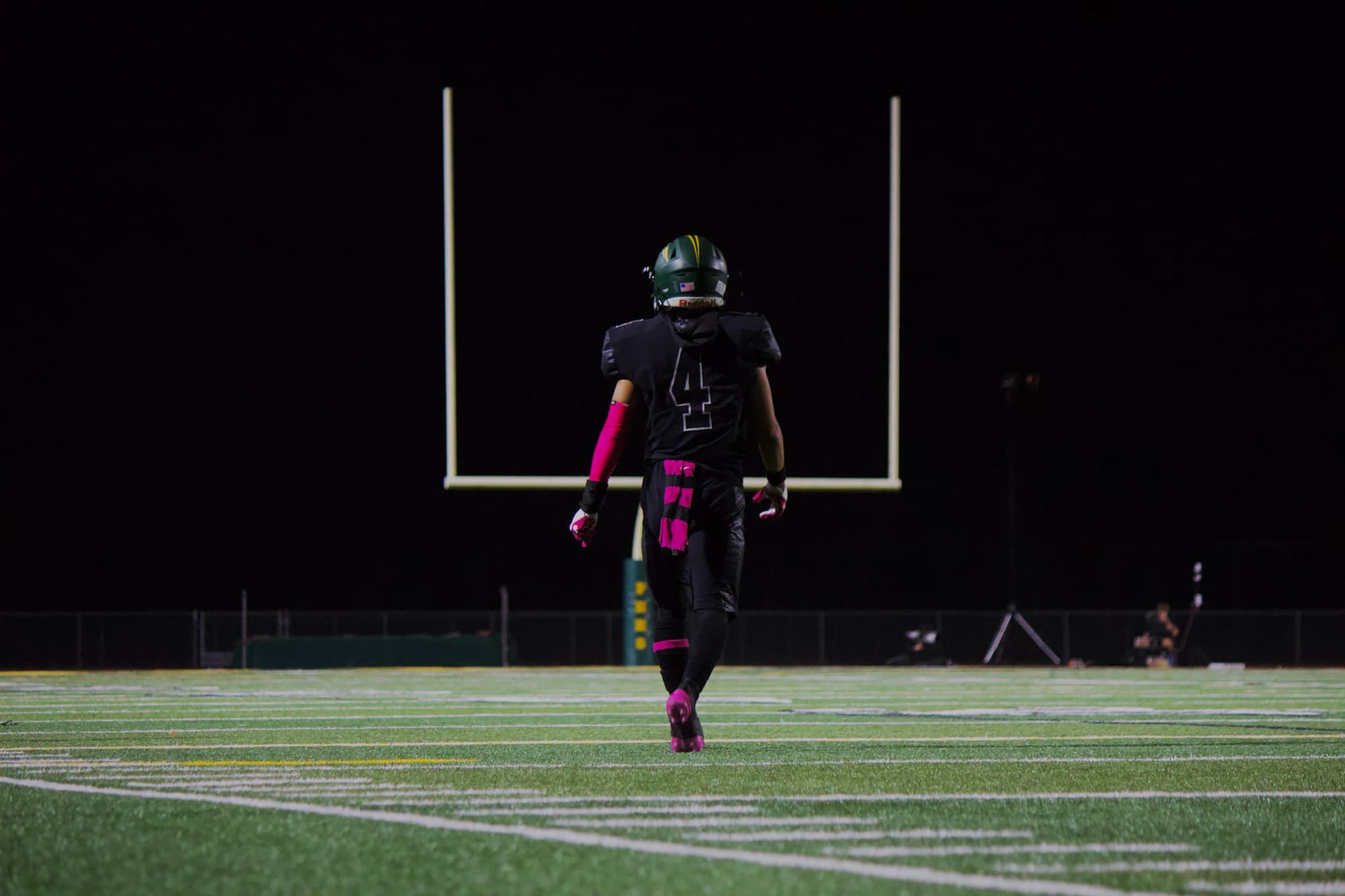A football athlete walking toward the goalposts at night